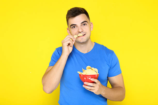 istock Young boy holding potato chips in bowl on yellow background 2210083598