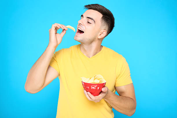 istock Young boy eating potato chips on blue background 2210083652