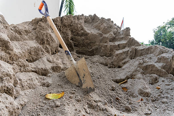 A shovel rests on a large sand pile outdoors with a nearby leaf perfect for construction or play sand.