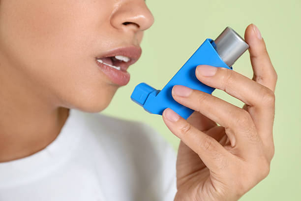 istock Young woman using asthma inhaler on light green background, closeup 2210085315