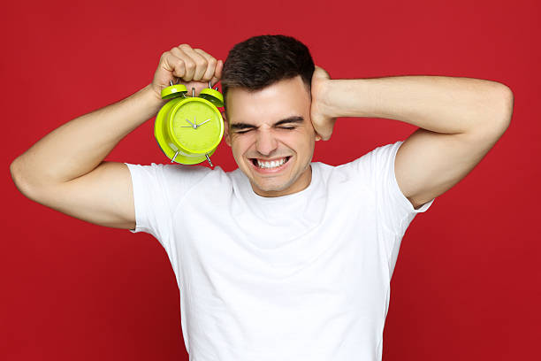 istock Young man with green alarm clock on red background 2210085780