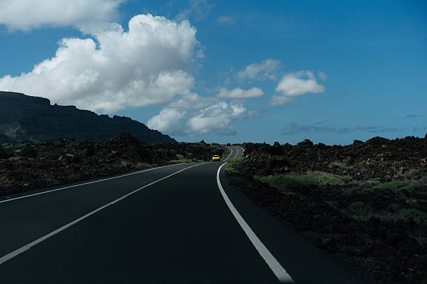 A road stretching into the distance on a volcanic island, under a blue sky dotted with clouds