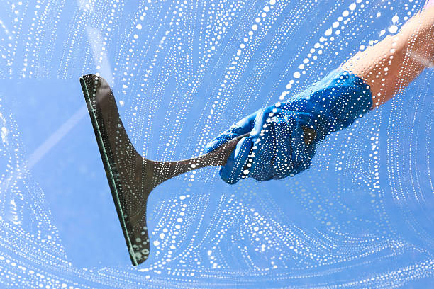 Woman washing window with squeegee tool against blue sky, closeup