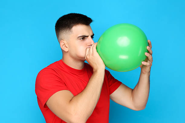 istock Yuong man blowing green balloon on blue background 2210085994