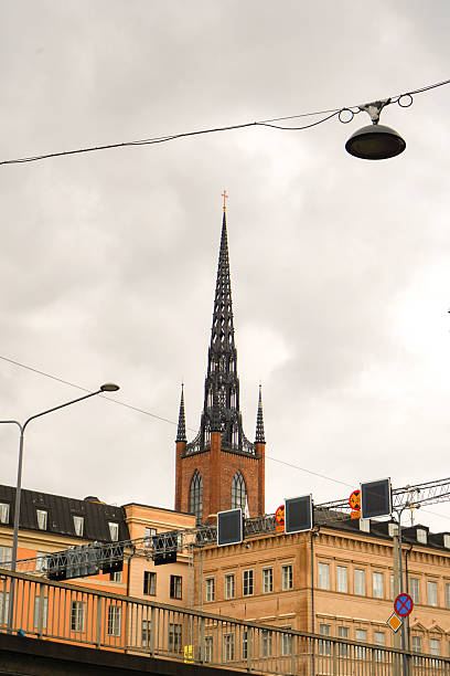 Black church tower leaning over yellow buildings with a street lite hanging on a electricity line above, Stockholm, Sweden