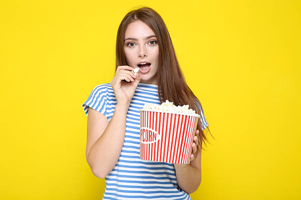 istock Beautiful girl eating popcorn on yellow background 2210092142