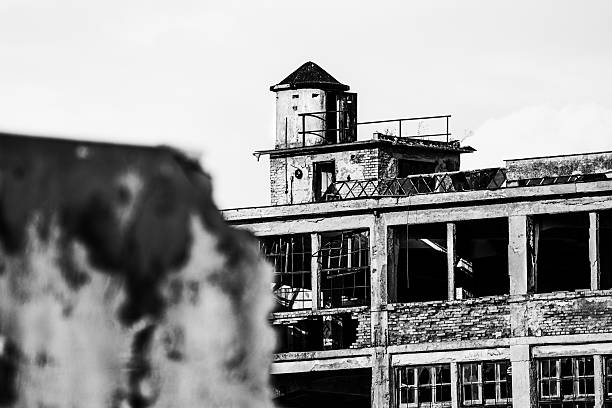 A stark black and white photograph captures the atmospheric ruins of an abandoned industrial building. The image highlights the textures and structures left behind, telling a story of a forgotten era.
