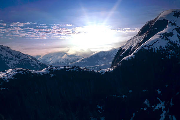 Aerial view of the Alaskan mountain range, snow capped with sun setting on horizon.