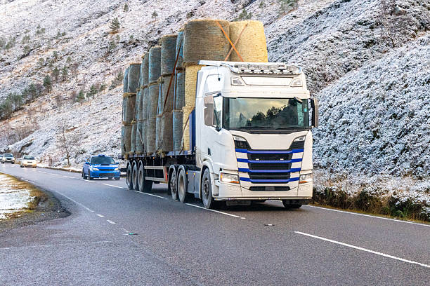 A large heavy goods vehicle travelling through the Scottish mountains to deliver large hay bails for animals to feed on.