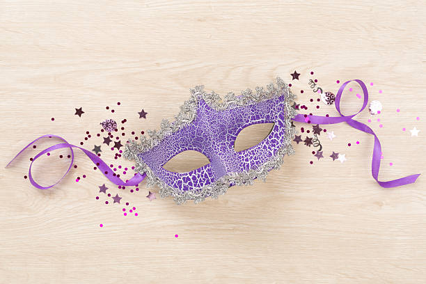 Bright carnival mask with confetti on wooden background, top view
