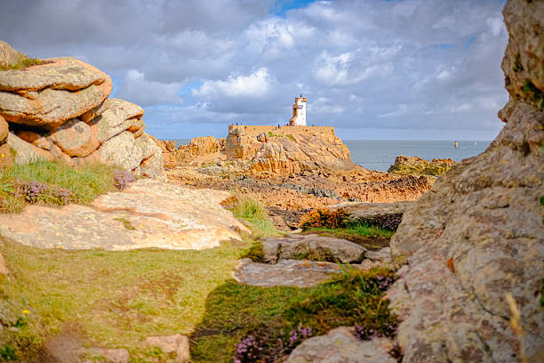 A small lighthouse off the Main island and red cliffs in the foreground. Taken on a partly sunny summer day, Brehat Island, Brittany, France.