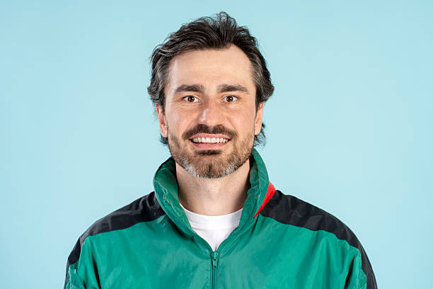 Portrait of a cheerful paramedic smiling and wearing a green jacket on a light blue background, conveying confidence and professionalism in healthcare. Advertisement concept