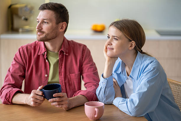 istock Smiling young couple staring into the distance while having tea and breakfast together in kitchen 2210151865