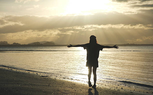 istock Silhouette of a woman open arms while strolling on the beach 2210153487