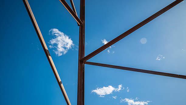 Industrial Steel Framework Construction with Geometric Patterns Against Bright Blue Sky with White Clouds Showcasing Modern Architectural Engineering
