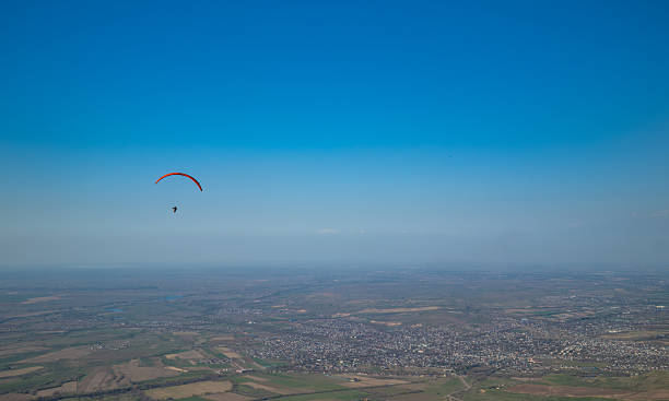 Paraglider with orange wing soaring against clear blue sky backdrop