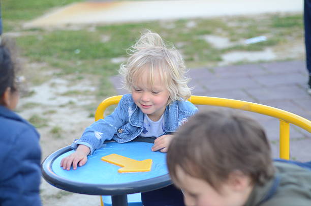 Happy children spinning on a roundabout in a playground. The kids exhibit joy and excitement, enjoying their playtime together. Green grass and a paved area surround them