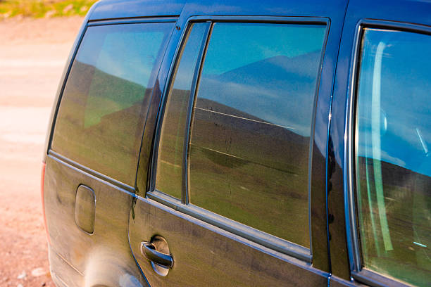 Rear view of a black vehicle covered in dust, with tinted windows reflecting the outdoor surroundings.