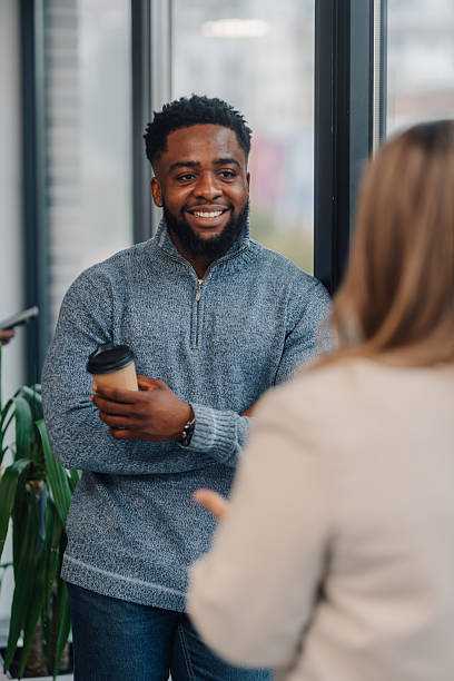 istock Smiling businessman holding coffee cup talking with coworker in office 2210163741