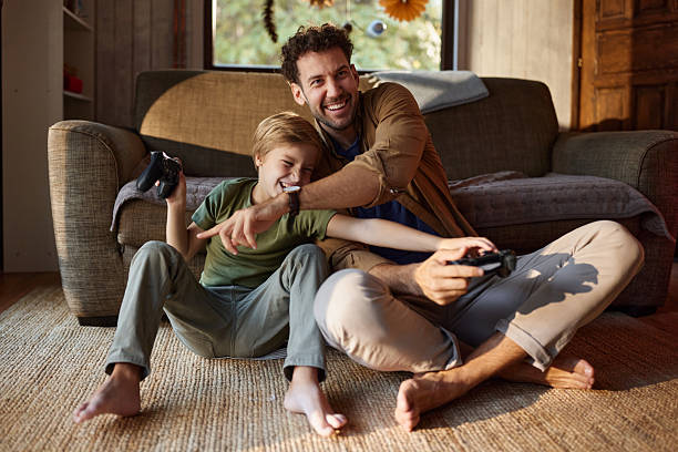 Happy father and son having fun while playing video games at home. stock photo