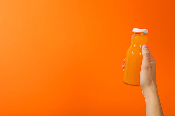 istock Glass bottle with juice in hand on orange background, space for text 2210167065