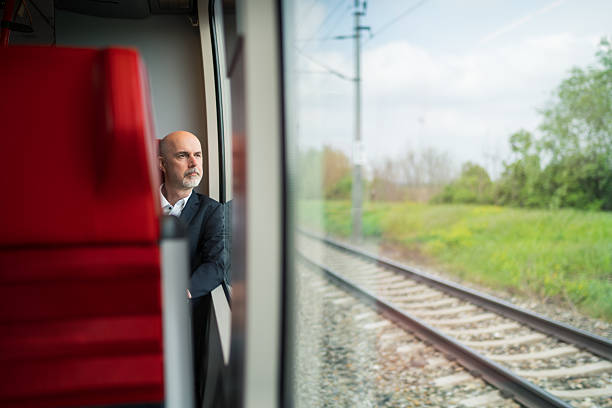 sustainable travel, one mature adult business man sitting in train looking out of the window, commuting to work, thoughtful, shallow focus on person
