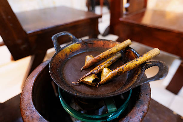 Rustic batik wax melting station surrounded by wooden stools in a traditional workshop in Solo, Indonesia. The pot contains melted wax and canting tools, reflecting the preparation process in batik-making culture.