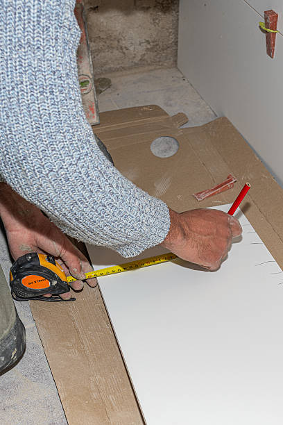 istock Construction worker taking measurements of ceramic tile using tape measure and marking with pencil during renovation or installation work 2210176199