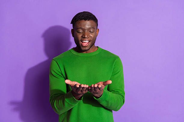 istock Young man gesturing with hands while smiling, dressed in a green sweatshirt against a vibrant purple background 2210179699