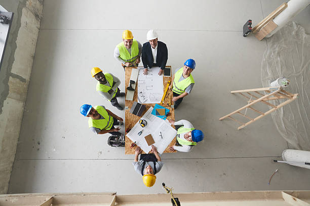 istock Above view of happy architect and manual workers working on plans at construction site. 2210181163