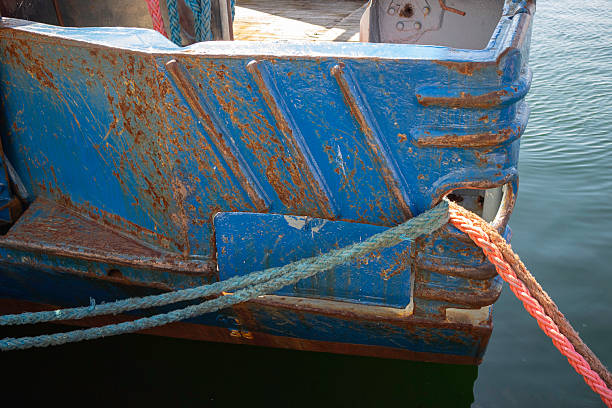 A blue boat with a rusty bottom and a red rope tied to it. The boat is in the water and he is old