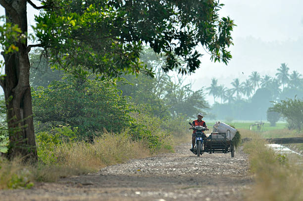 Aceh Besar, Indonesia - 20 Apri 2023: Farmer walking on the road using an old motorbike