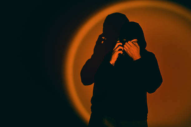 Mysterious criminal hiding face in dark room with orange spotlight