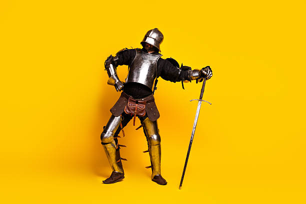 istock Young man dressed as a medieval knight posing against a vibrant yellow background in full armor with a sword 2210193098