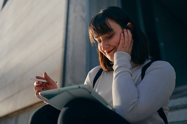 istock Young woman drawing on tablet outside a building 2210196208