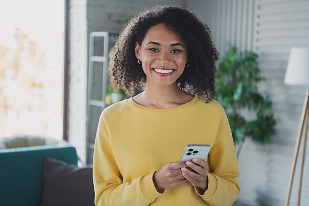istock Young woman in yellow sweater joyfully using smartphone indoors 2210196664