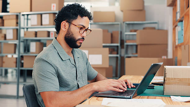 istock Office, logistics and man typing on laptop for sales order, ecommerce or distribution in small business. Computer, shipping and worker in startup for supply chain email, stock procurement and serious 2210198254