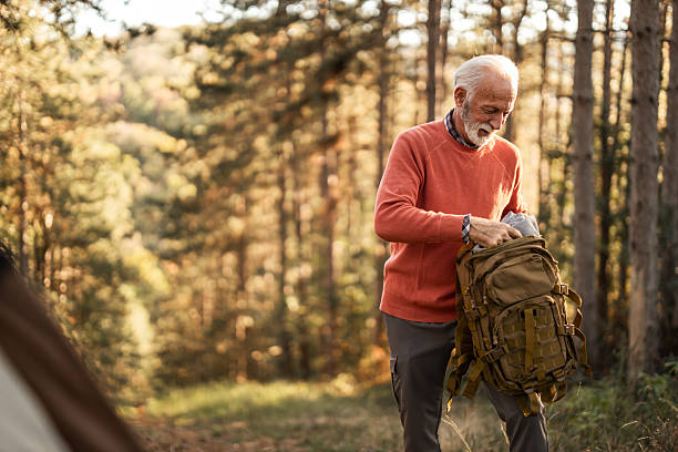 istock Senior Man Unpacking Backpack in Forest During Daytime Camping Trip 2210198472