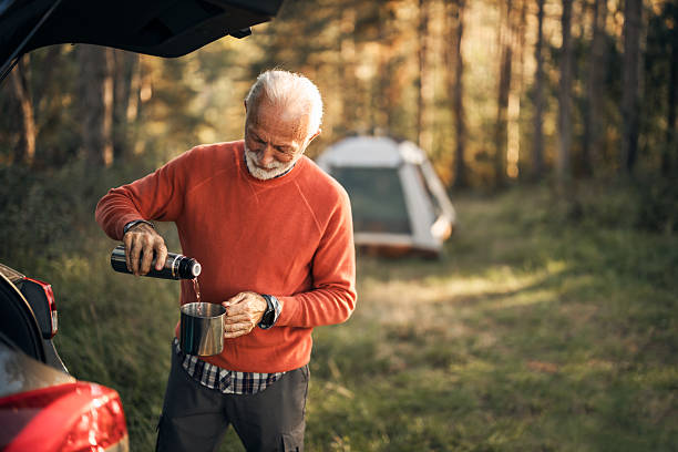 istock Senior Man Enjoying Camping and Pouring Tea Outdoors in Forest 2210198512