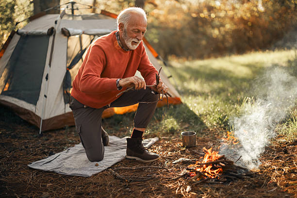 istock Elderly Man Camping in Forest Lighting a Campfire Beside Tent 2210198553