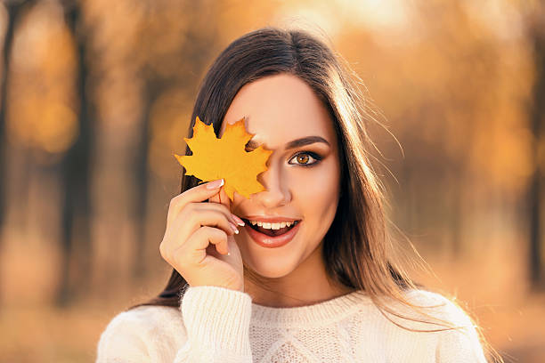 istock Beautiful woman holding maple leaf in autumn park 2210198607