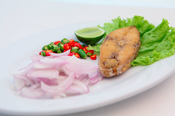 Salted fish, Crispy Mackerel with Fish Sauce, Crispy mackerel fillet fried with fish sauce, served with sliced red onion, chopped chili, fresh lime, and green lettuce