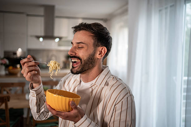 istock Happy man eating noodles from a bowl in his kitchen 2210209074