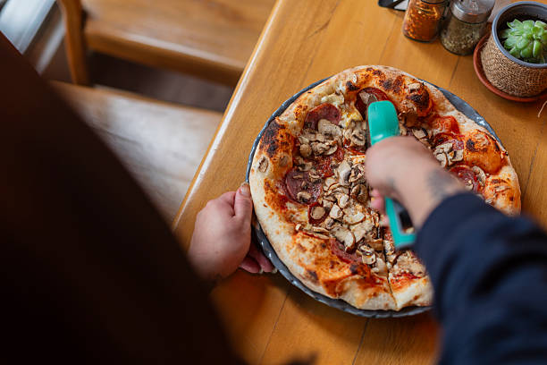 Woman's hand with a knife cut the pizza. Delicious pizza Margarita. Take out freshly baked italian pizza being held in a box, close up. Italian traditional classic pizza Margarita. Fast Food.