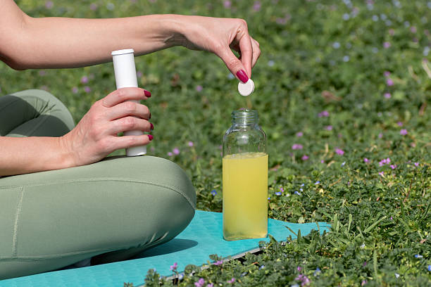 istock Sportswoman dissolving an effervescent tablet in juice while sitting on yoga mat during outdoor exercise on hot summer day. Refreshment, hydration, vitamins and health supplements in sports 2210211301