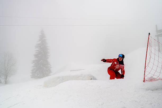 A snowboarder wearing a red outfit and goggles is seen performing an action move in a snowy mountain environment on a cloudy day. This dynamic image showcases the thrill of winter sports, featuring skillful movement amidst scenic snow-covered landscapes.