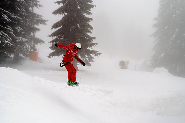 istock Snowboarder navigating a snowy slope amidst fog and tall pine trees 2210213436