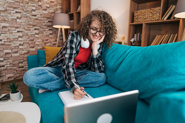 istock Young student taking notes while following online lesson at home 2210224026