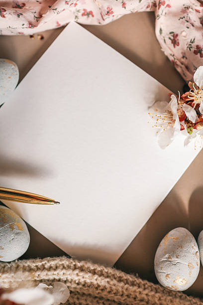 istock Flat lay with a blank white square card surrounded by decorative Easter eggs, blooming branches, golden pen, soft knitted textile, and floral fabric â perfect for greeting or invitation design 2210224477
