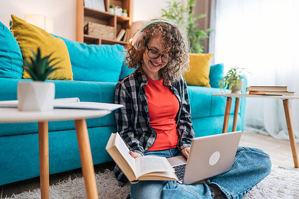 istock Young woman studying at home using laptop and textbook while wearing headphones 2210225223